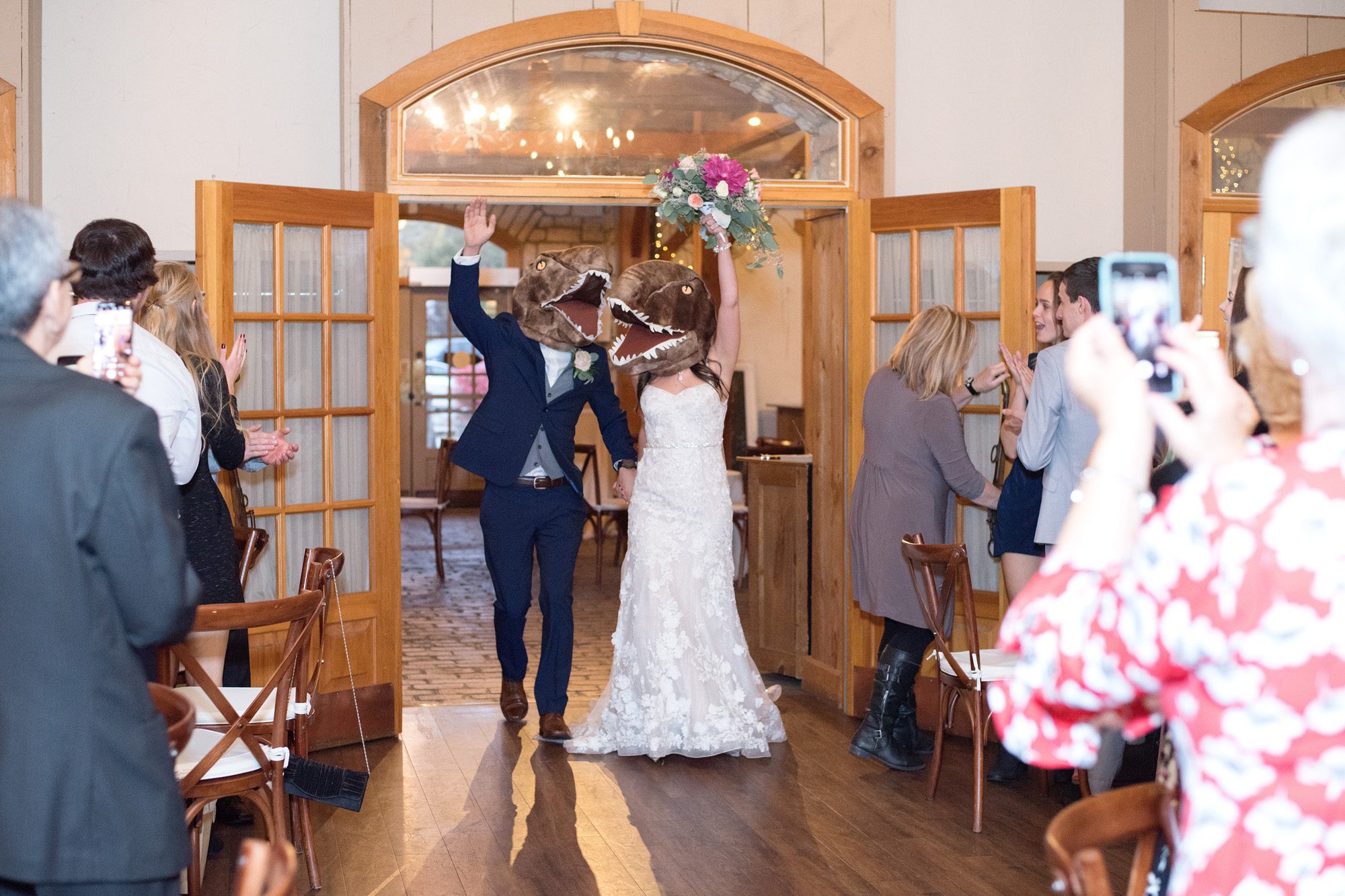 Bride and groom wearing dinosaur masks while entering their reception at Bellamere Winery.