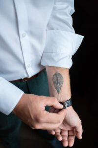 Groom fixing watch with leaf tattoo on forearm.