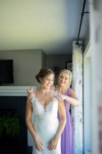 Brides maid of honour putting on bride's necklace.