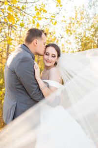 Groom kissing bride cheek with veil flowing around in Cambridge.