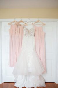 Wedding dress and bridesmaids dresses hanging together on closet.