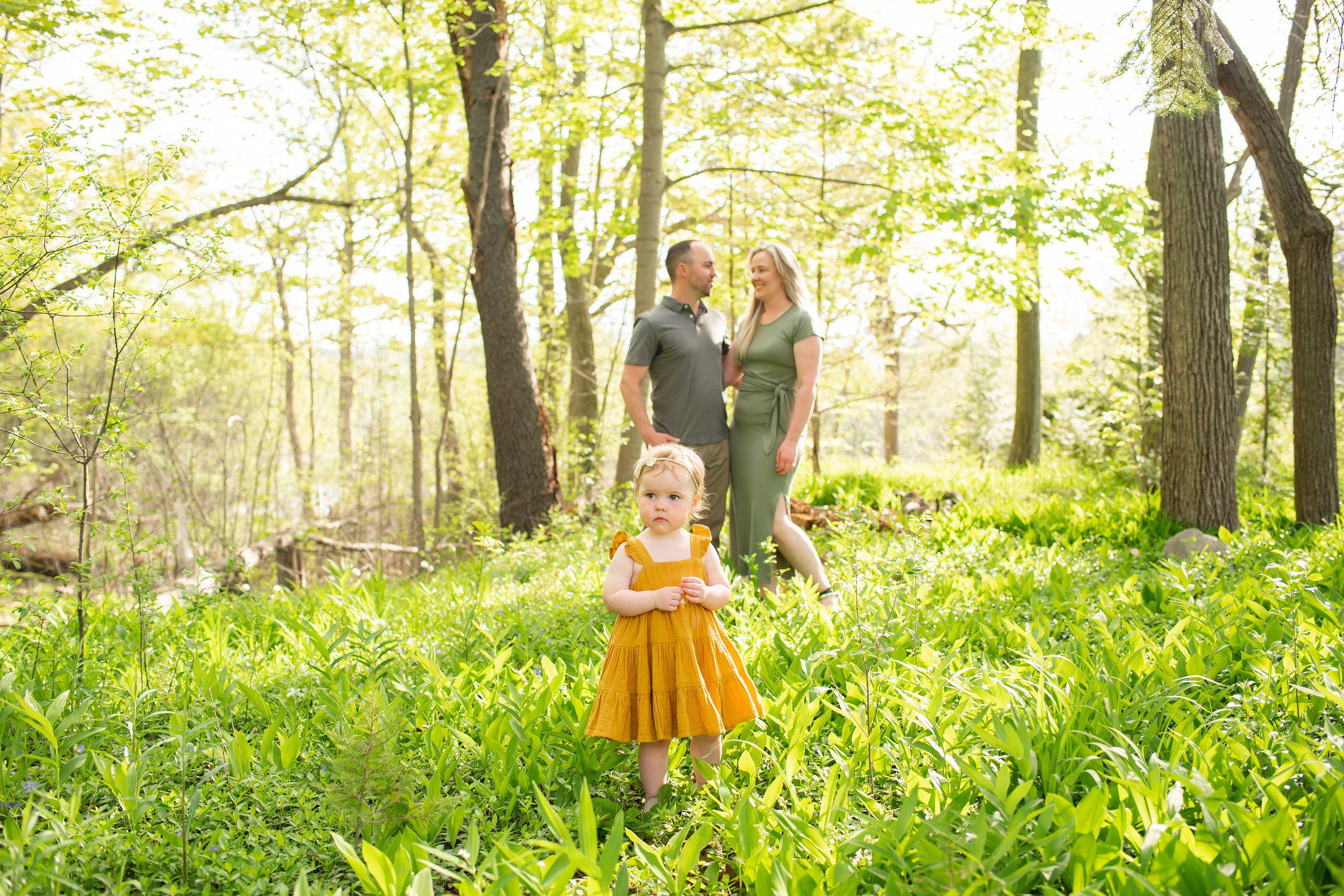 Little girl in foreground while parents look at each other in background at Springbank Gardens