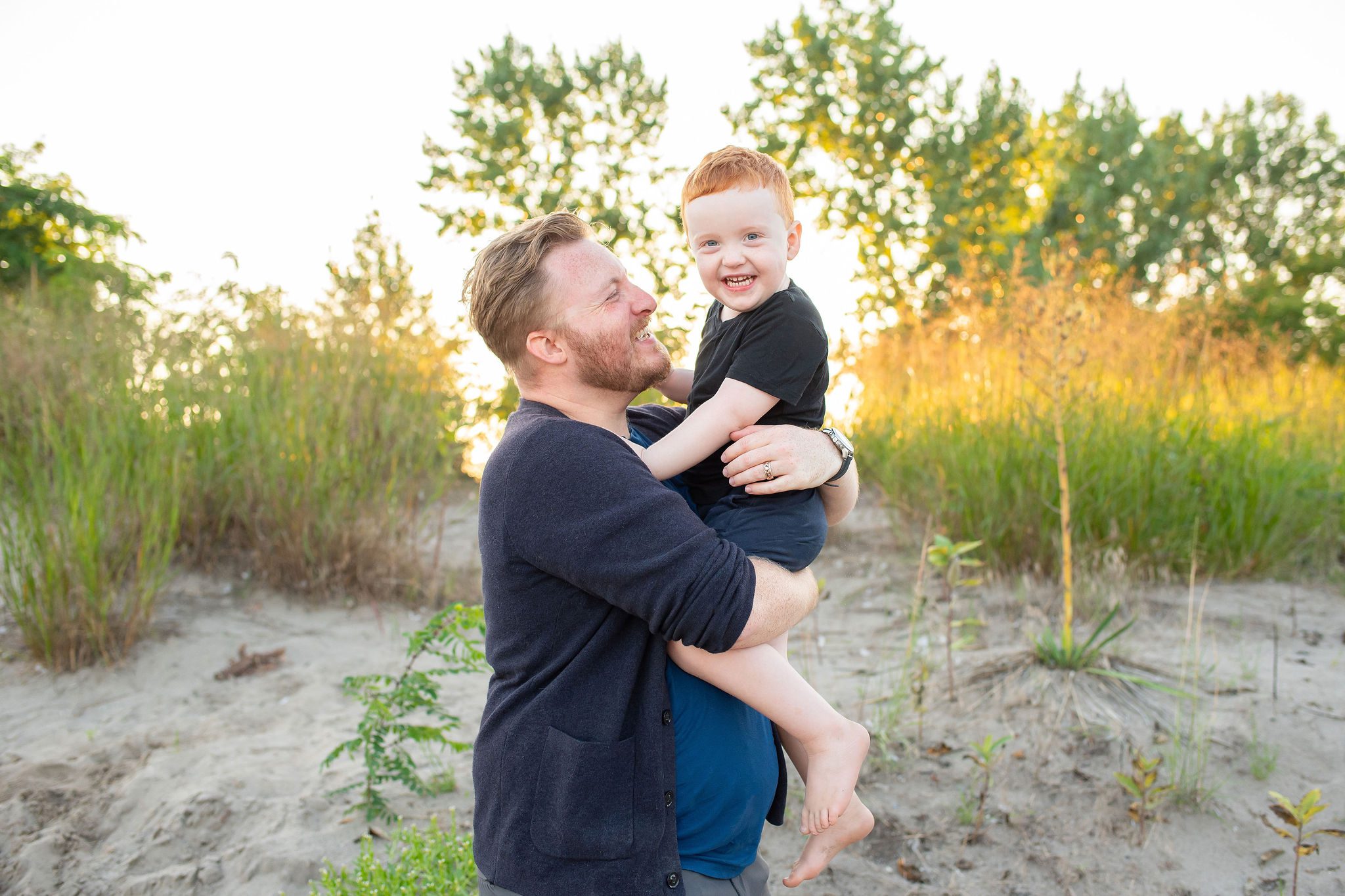 Dad holding son and smiling up at him at the beach.