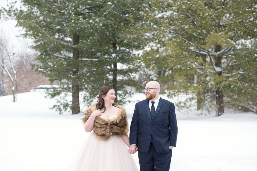 bride and groom holding hands smiling at each other at their winter wedding