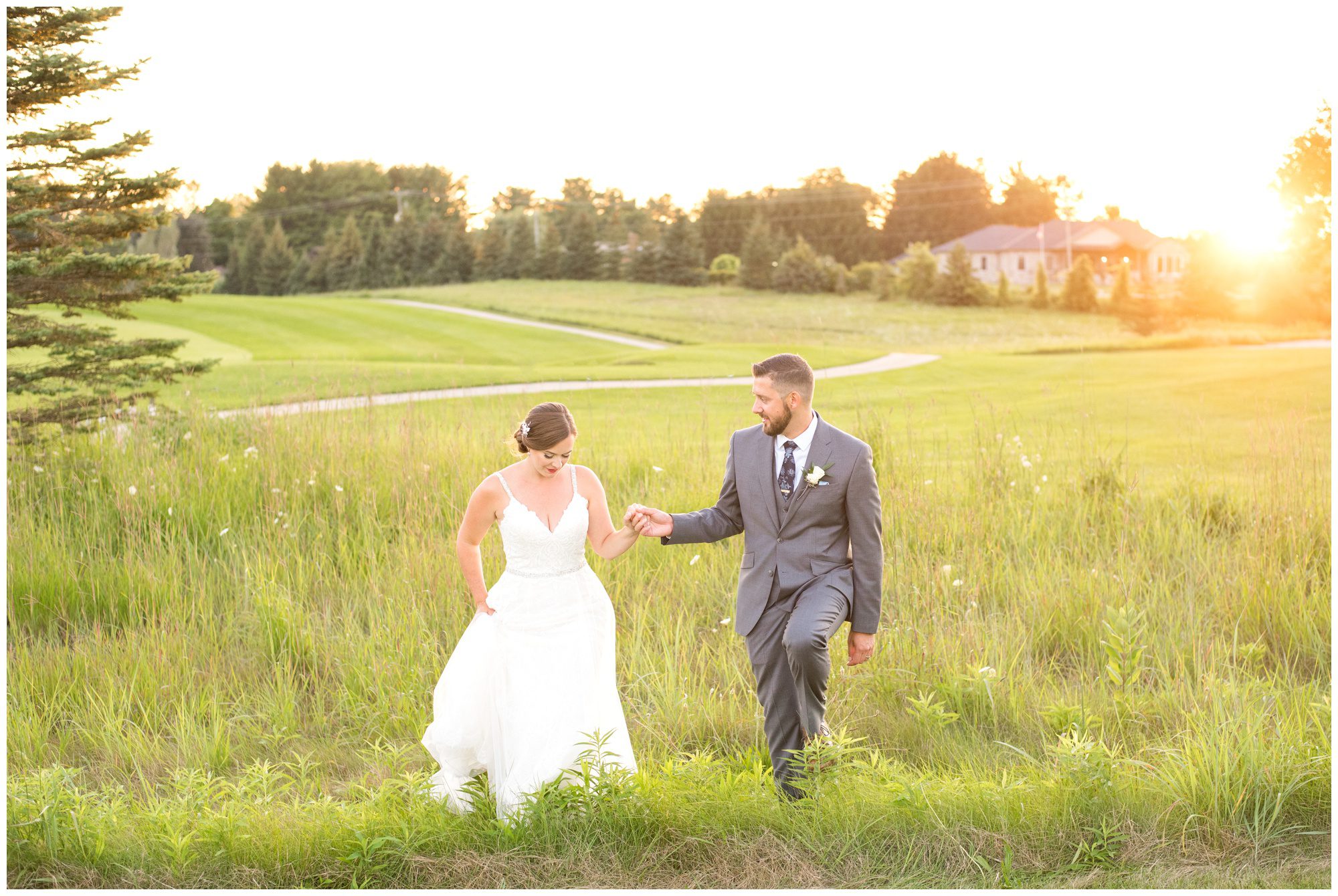Bride and groom walking hand in hand through field at golden hour
