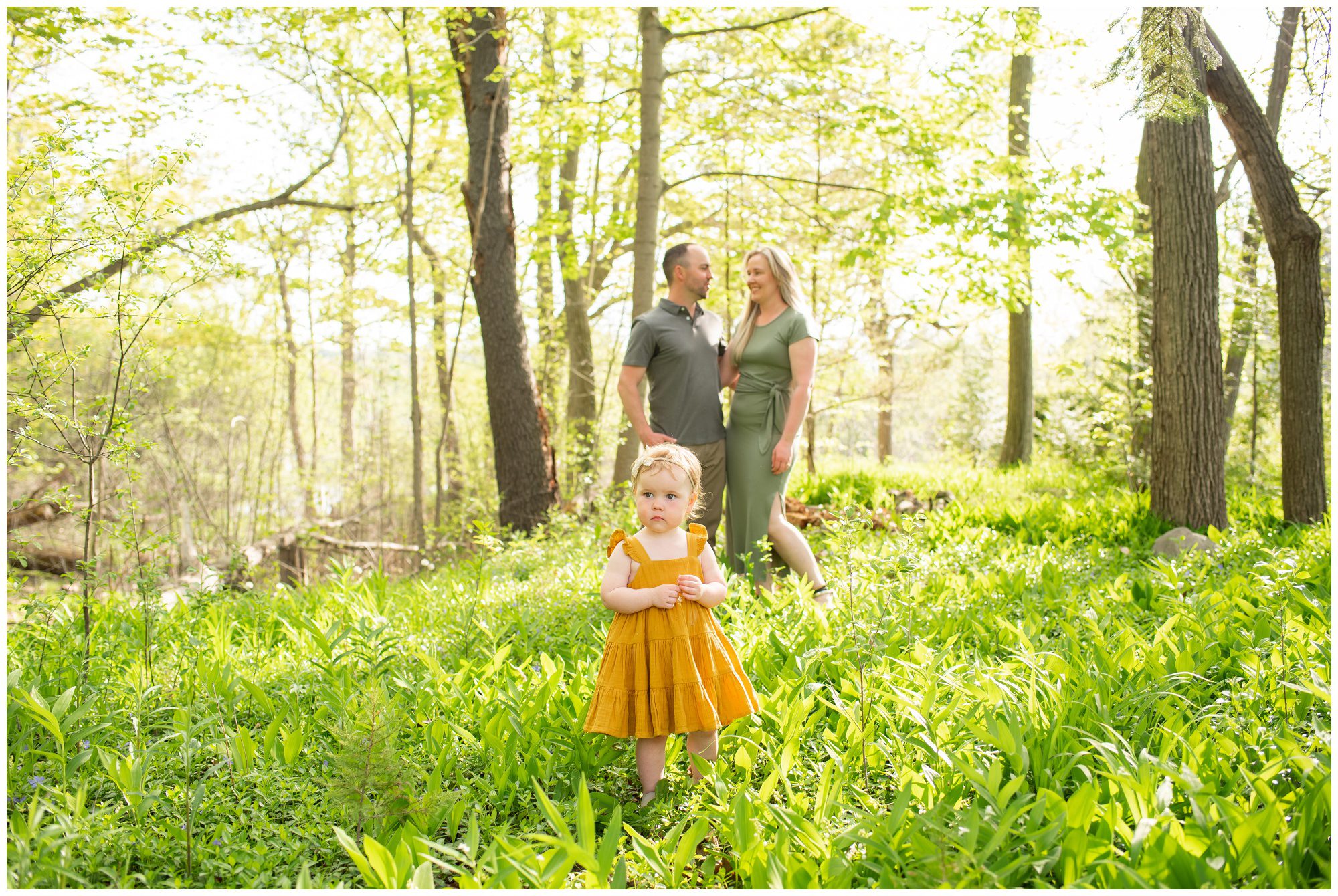 Little girl standing in the grass with her parents in the background at Springbank Gardens