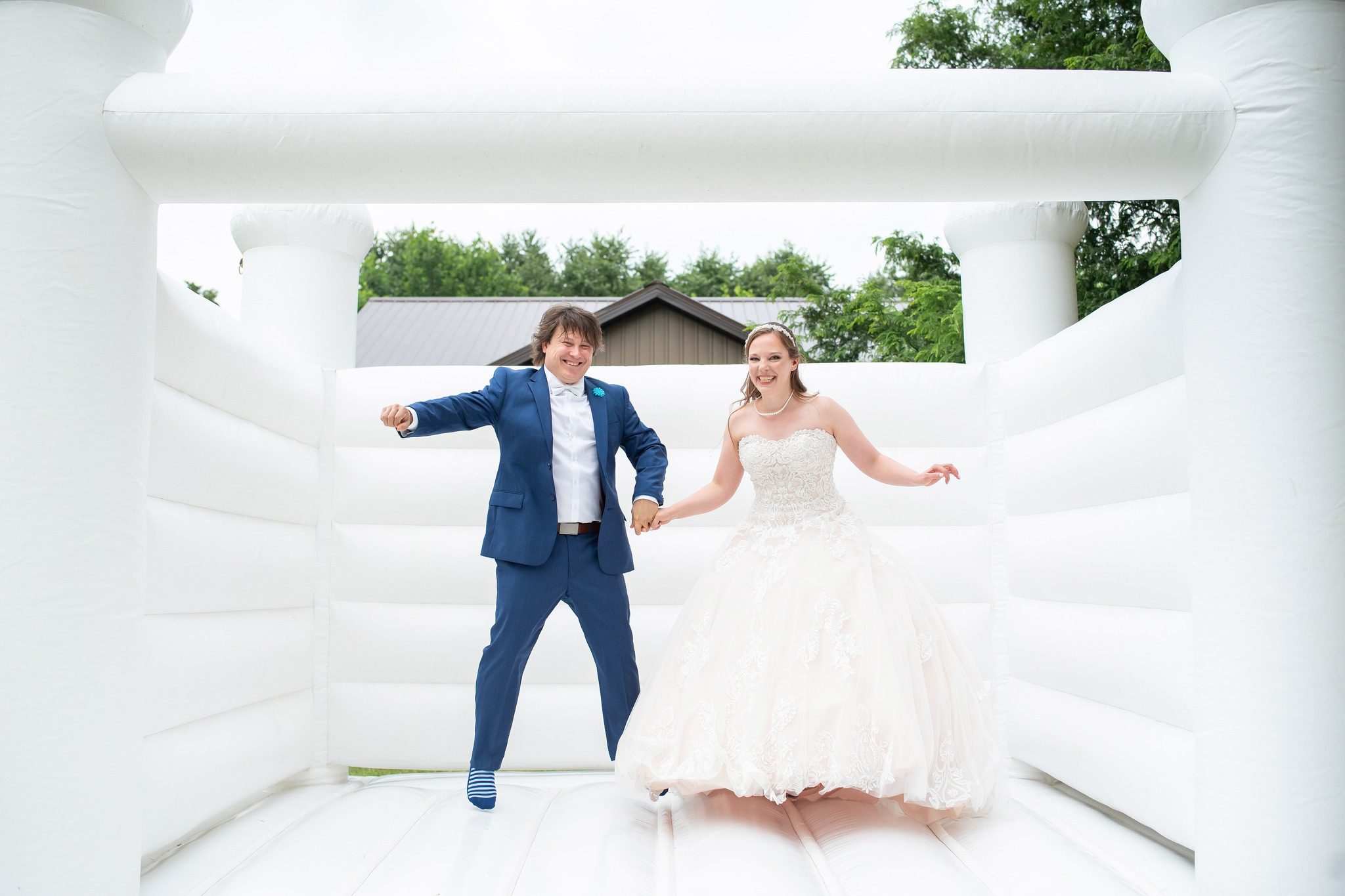 bride and groom jumping on a white castle bouncy house together.
