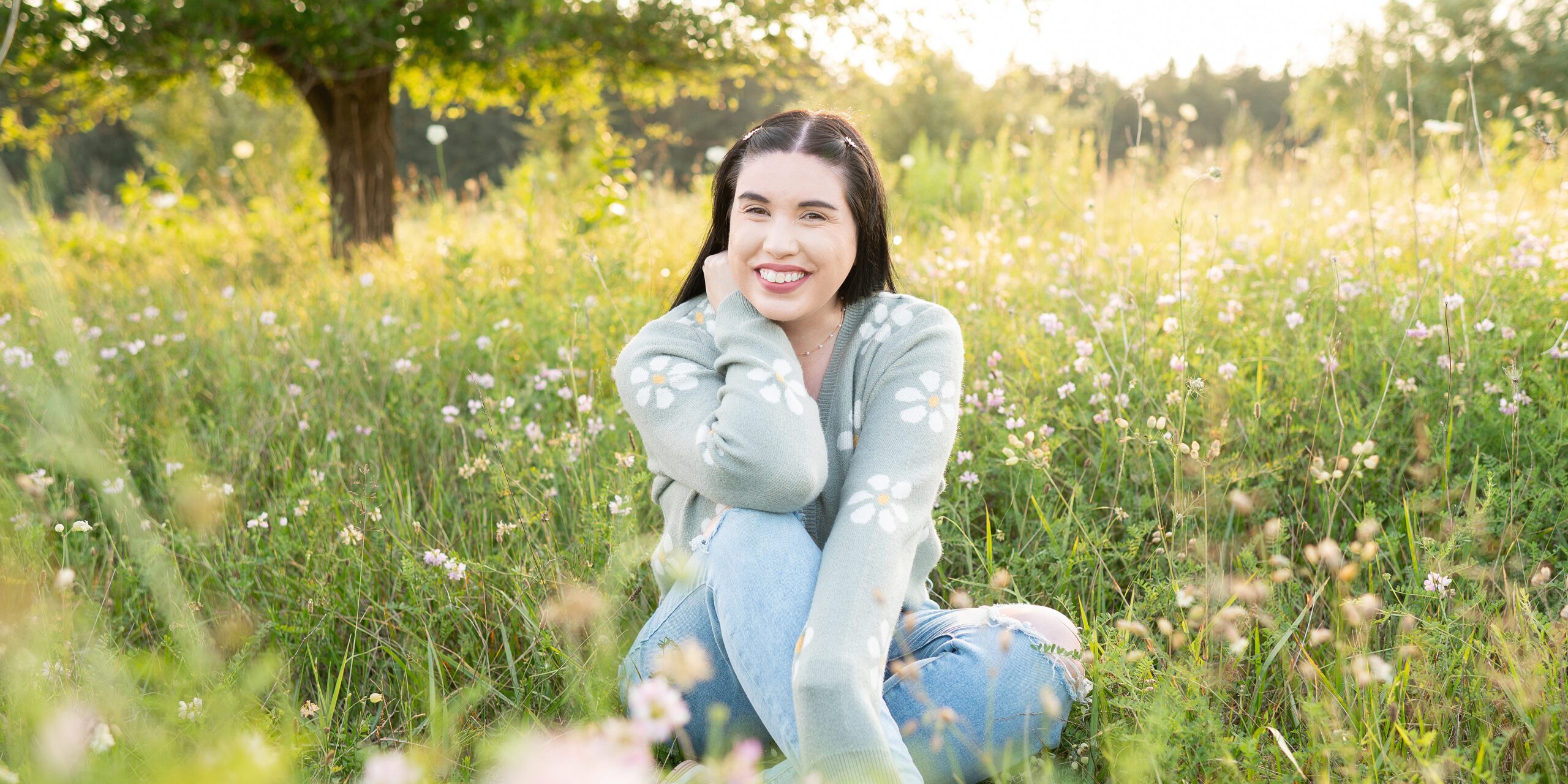 Michelle of Michelle A Photography sitting in a wildflower field smiling at the camera.