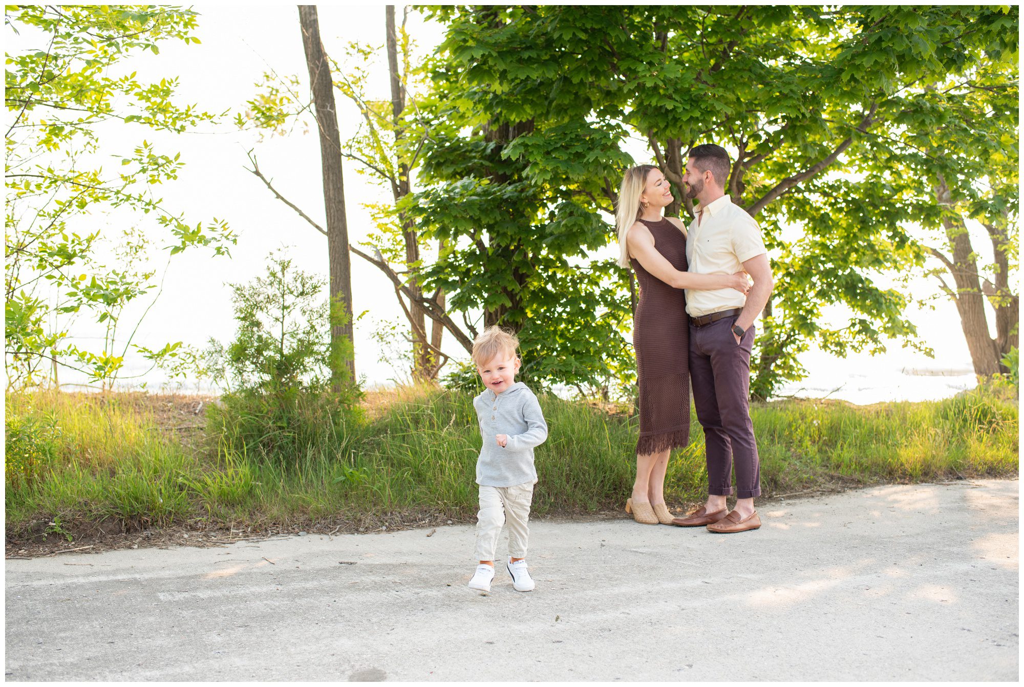 Little boy running towards camera while his parents hug in the background at Bayfield Beach