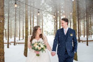 Bride and Groom walking under falling snow at Crescent Hill Acres.
