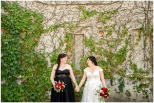 Two brides holding hands looking at each other and smiling at The Old Court House in London Ontario.