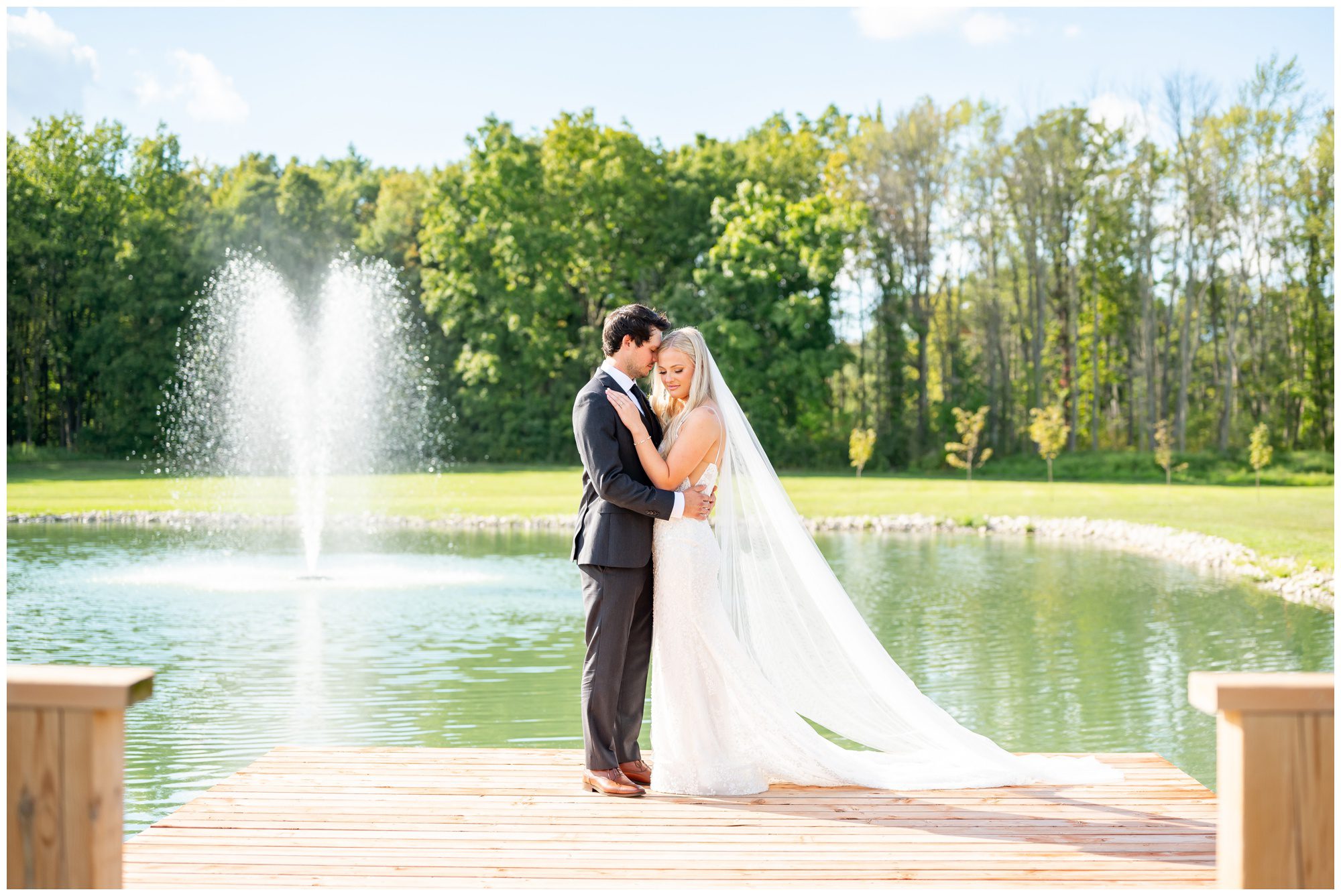 Bride and groom on dock in front of pond and fountain.