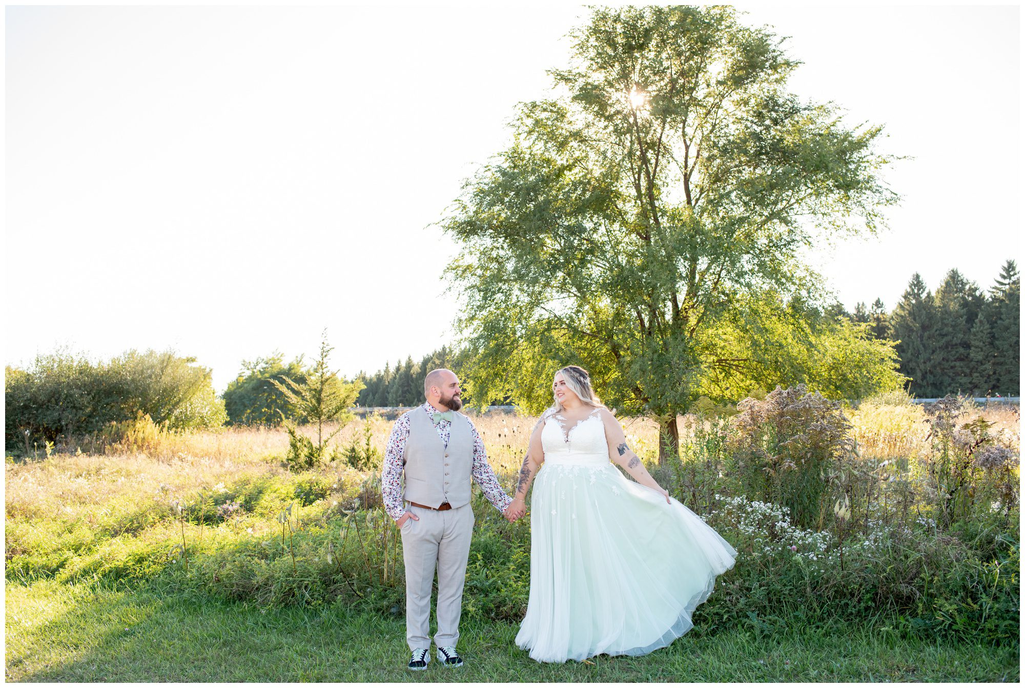 Bride and groom standing hand in hand in front of a field at Fanshawe Conservation Area in London Ontario.